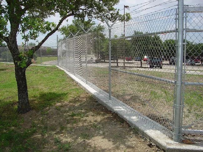 Chain link fence set on a concrete mow strip beside a shaded lawn