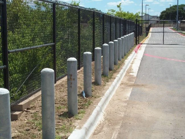 Black chain link fence and concrete bollards lining a paved access drive