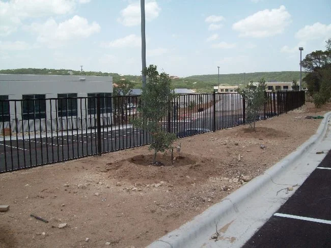 Black iron fence running along a commercial building and its parking lot