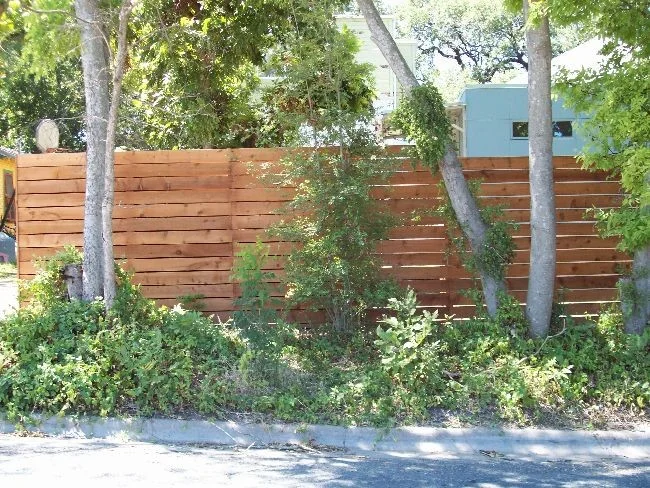 Horizontal cedar privacy fence built between mature trees along a sidewalk