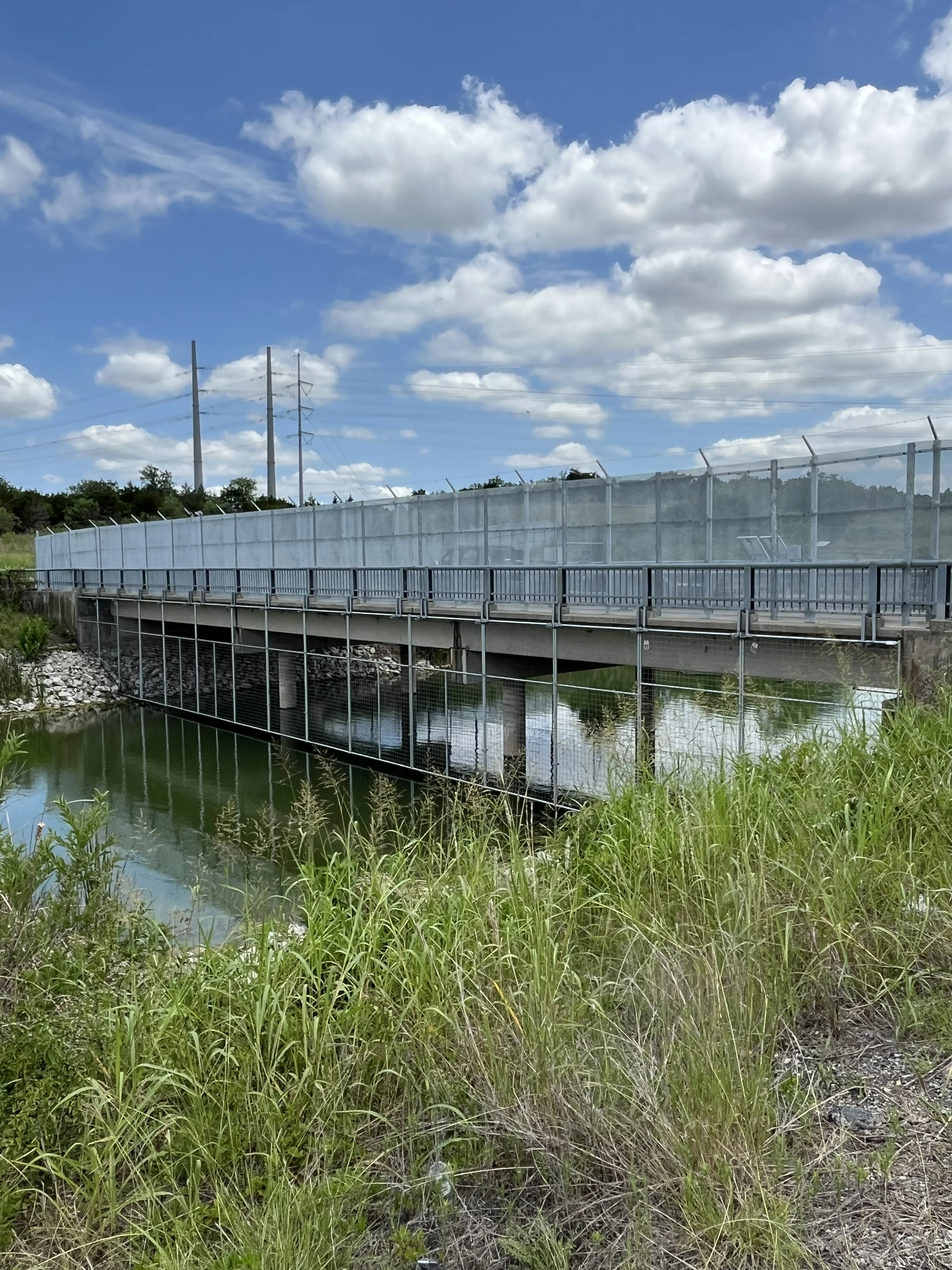Tall chain link safety fencing along both sides of a concrete bridge over water