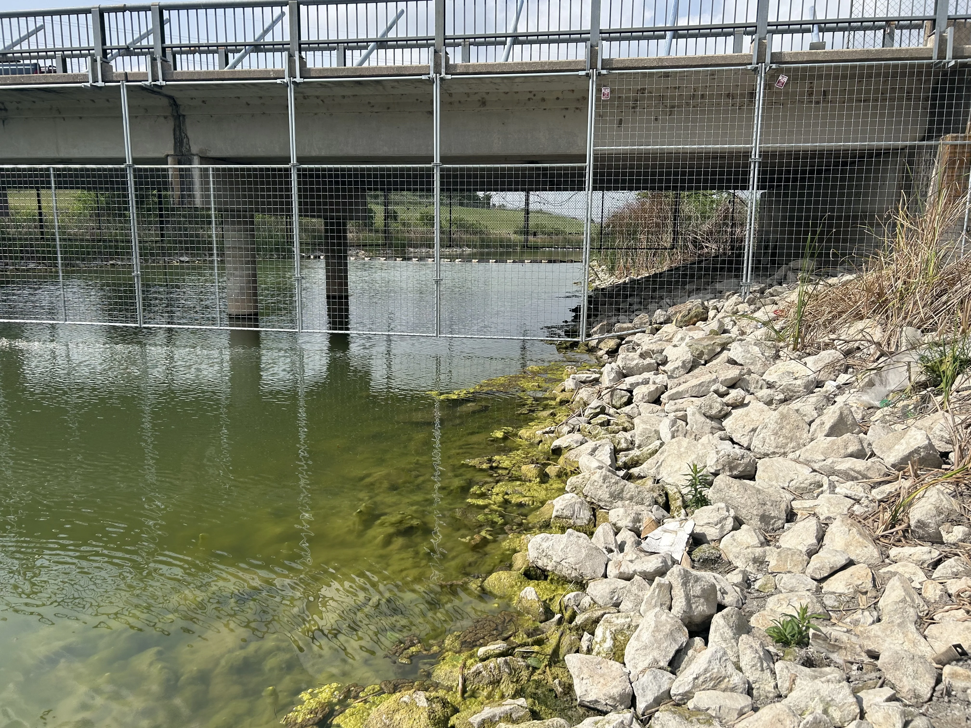 Chain link screening beneath a bridge deck above a rock lined bank