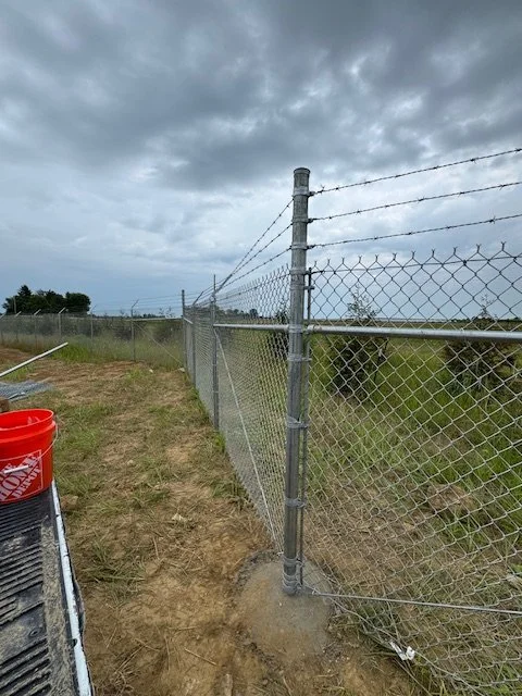 Chain link fence with a barbed wire extension arm running up a hillside