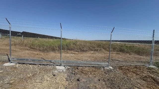 Chain link perimeter fence topped with barbed wire at an industrial site