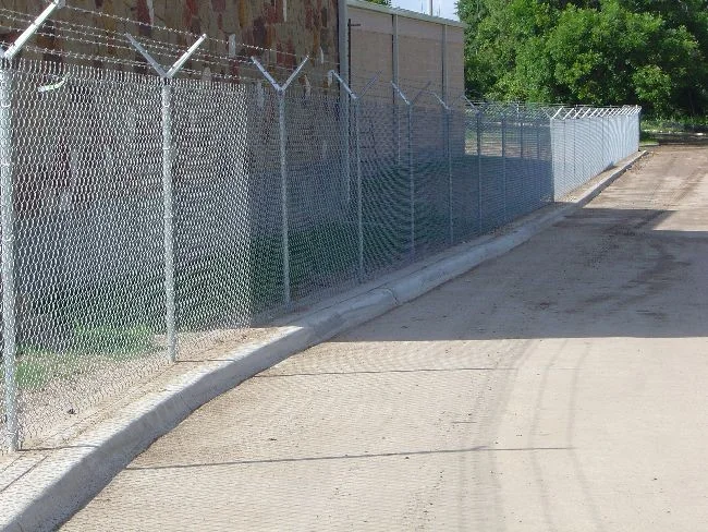 Galvanized chain link fence topped with barbed wire along a commercial driveway
