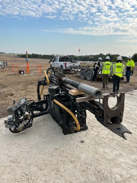 Crew in high visibility gear with a hydraulic post driver staged on a job site