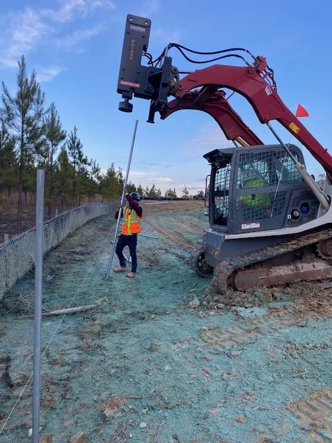 Crew running a skid steer post driver along a fence line at the treeline