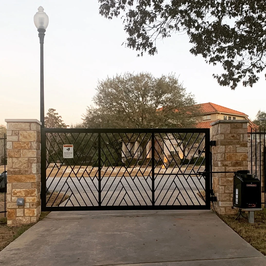 Custom ornamental iron driveway gate with chevron panels set between stone columns