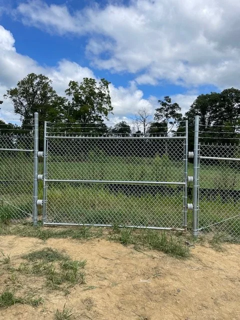 Galvanized chain link fence and swing gate across a grassy field