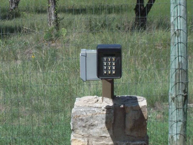 Keypad entry pedestal mounted on a stone base beside a ranch gate