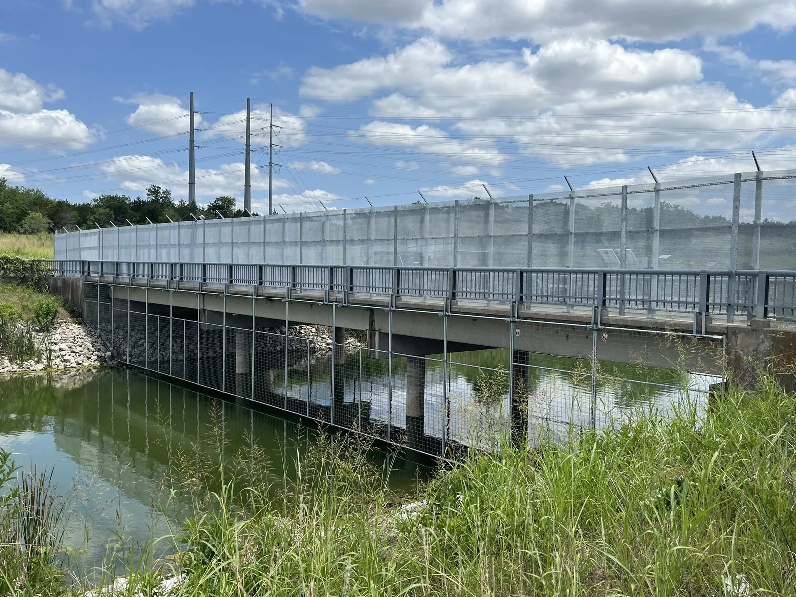 Highway bridge fitted with tall chain link safety screening above a waterway