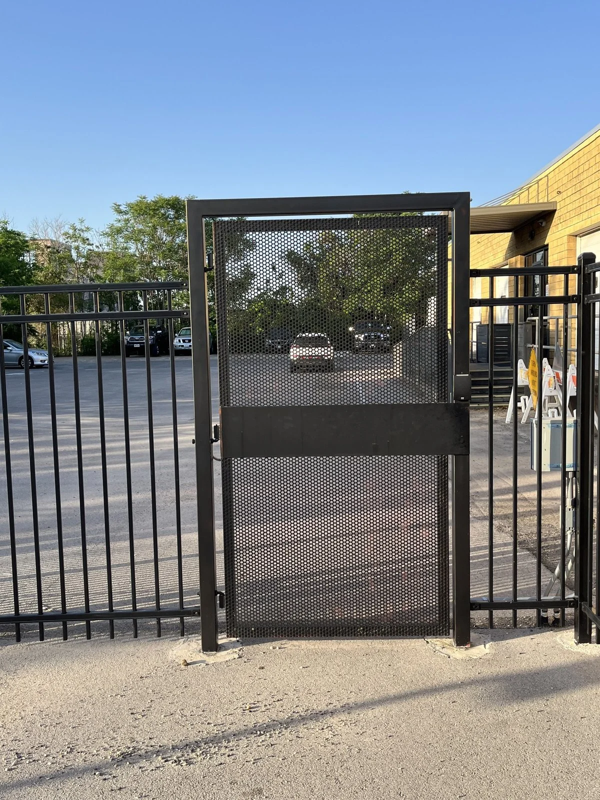 Mesh panel pedestrian gate standing open in an ornamental iron fence line