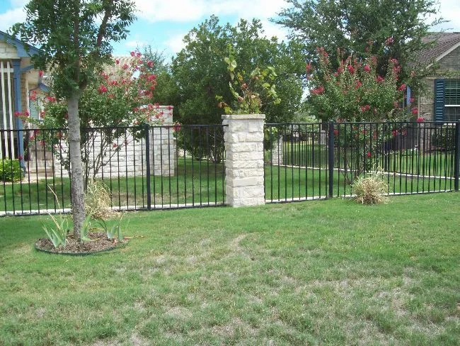 Black ornamental iron fence with a stone column in a landscaped front yard