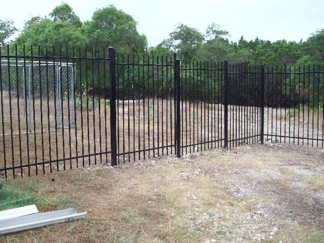 Black metal fence along a cleared commercial lot beside storage buildings