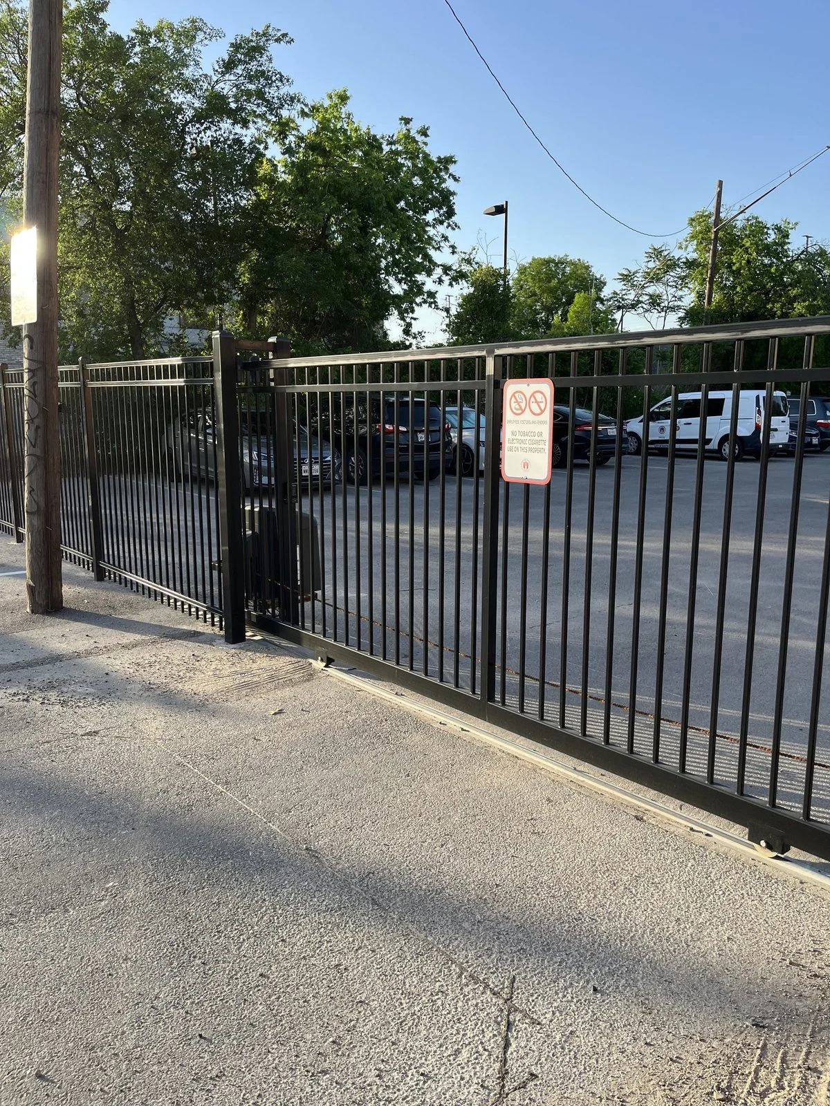 Black ornamental iron fence running along a sidewalk beside a parking lot