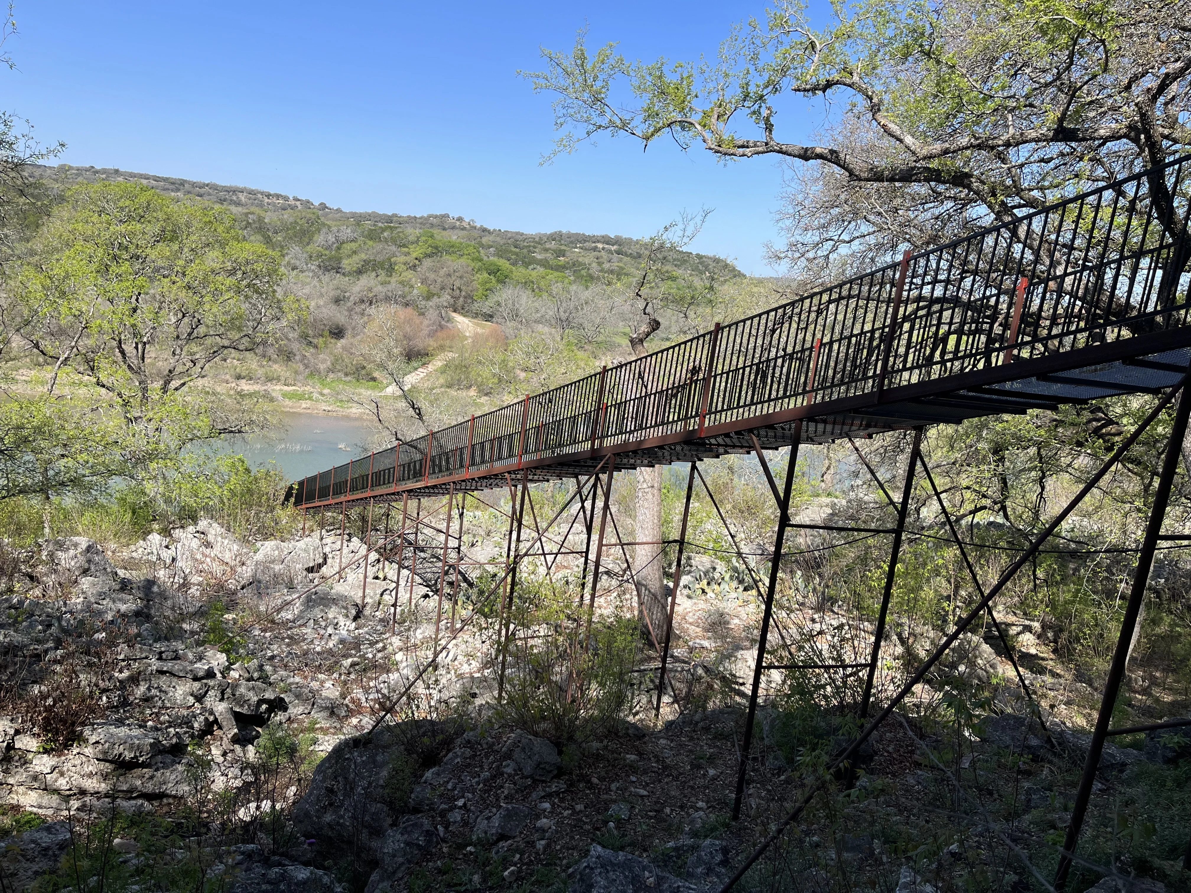 Steel pedestrian bridge with handrail fencing crossing a Hill Country river