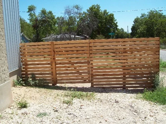 Horizontal cedar fence enclosing a gravel side yard between two buildings