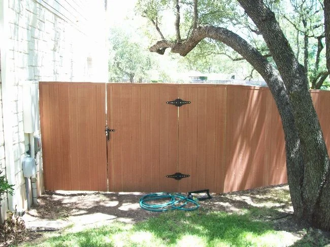 Stained wood privacy gate with black strap hinges beside a house