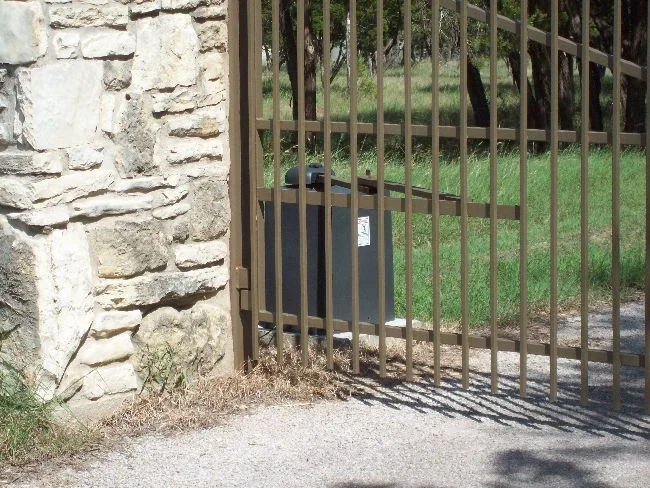 Iron driveway gate with a gate operator mounted beside a stone column