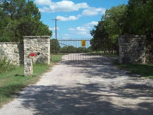 Iron ranch entry gate between stone columns at the head of a gravel drive