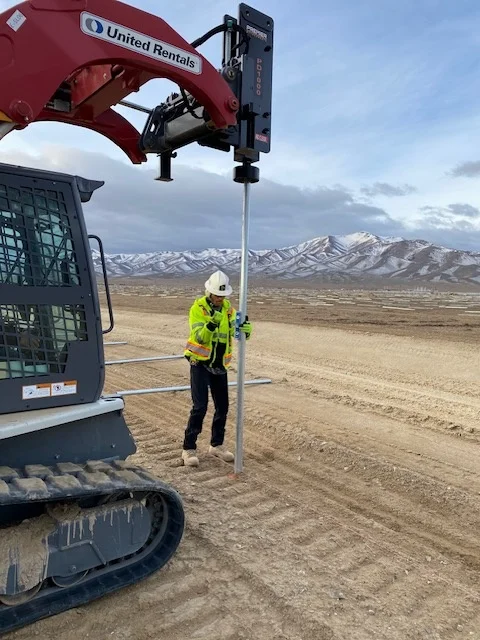 Crew member setting fence posts with a skid steer mounted post driver