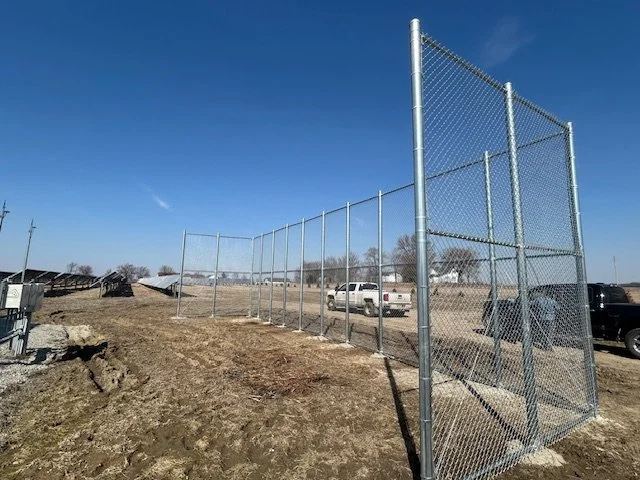 Tall galvanized chain link backstop fencing at the edge of a work yard
