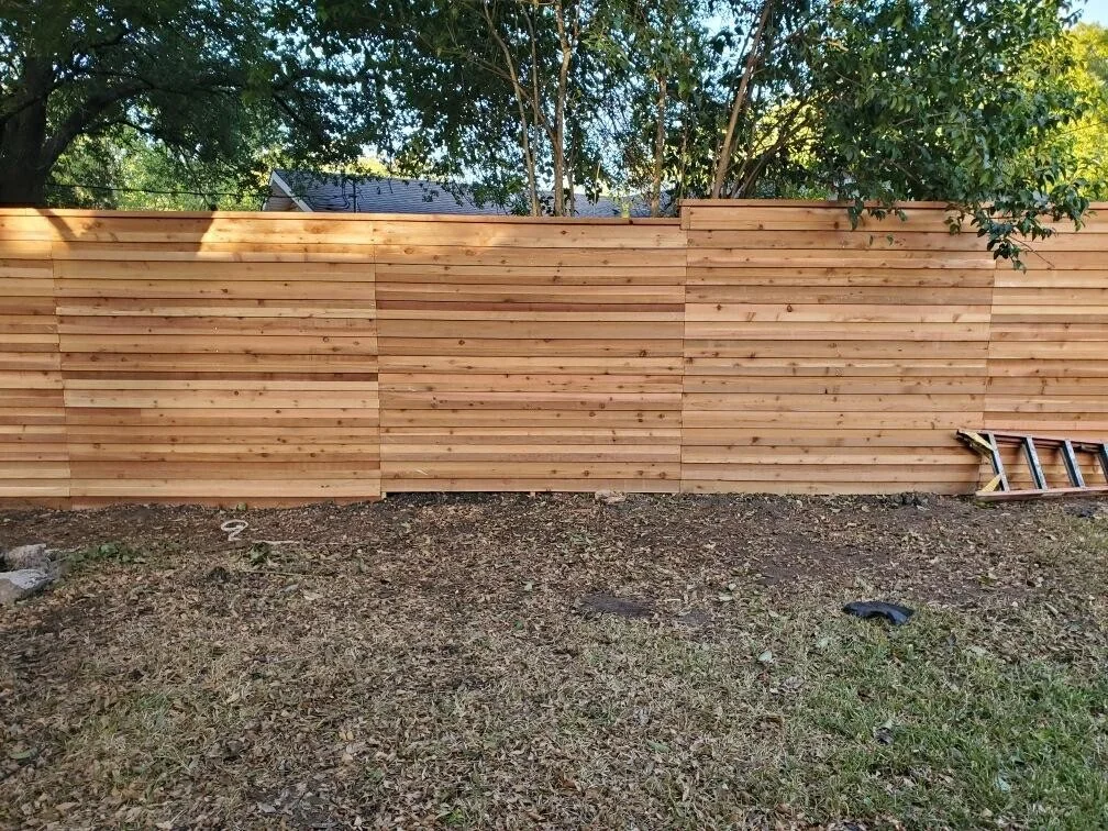 Tall horizontal cedar privacy fence along the rear boundary of a lot