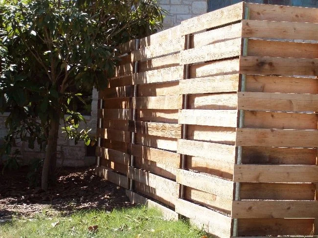 Horizontal cedar slat fence with open gaps built against a stone wall